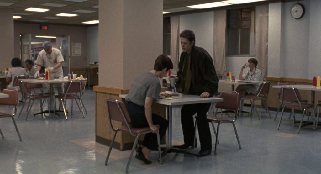End of the first shot of the sequence. The camera tracked with John and Marianne to a table. John is sitting down, Marianne is already seated.