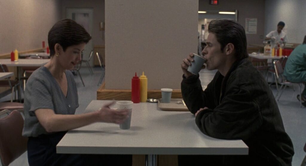 The second shot of the sequence. A standard medium shot of John and Marianne sitting at the table across from one another.
